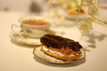eclair in chocolate glaze and a cup of tea on the table