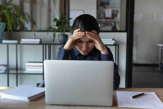 Stressed young indian ethnicity businesswoman stuck with hard task, looking at computer screen, Confused millennial female multiracial overload employee suffering from head ache, workaholic concept.