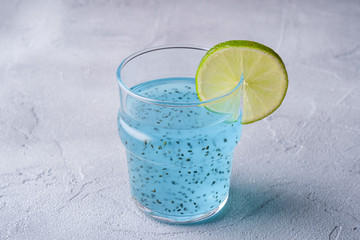 Tasty blue colored cocktail drink with basil chia seeds and citrus lime slice in glass, healthy summer beverage, stone concrete background, angle view