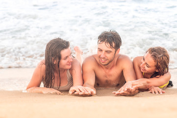 Fototapeta premium summer holidays concept. Young friends - Man and girls have fun on the beach, laying on the gold sand