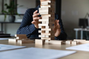 Close up young indian woman constructing tower with wooden bricks alone in office, sitting at...