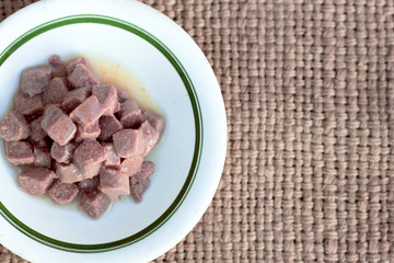 food for cats, pieces of meat or tuna in jelly, a bowl of canned food for pets stands on a mat on the floor, free space, favorite food for a pet