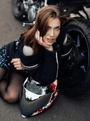 Fototapeta na wymiar Young cute female driver and dark modern bike. Urban powerfyl vehicle. Motosport hobby.