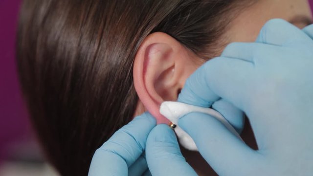 Doctor woman conducts ear piercing procedure for client.