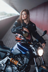 Fototapeta na wymiar The bridge road in sunlight. Pretty beauty girl with her own dark casual motorbike on the bridge. Motosport passion portrait.