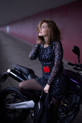 Naklejka na ściany i meble A nice looking girl with her casual modern bike. Urban motosport hobby. Brown-hair female driver.