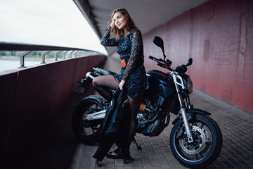 Fototapeta na wymiar A nice looking girl with her casual modern bike. Urban motosport hobby. Brown-hair female driver.