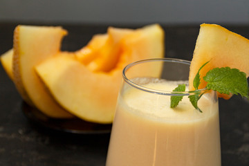Melon milk shake on a black background. Ripe sliced melon is lying nearby. The smoothie glass is...