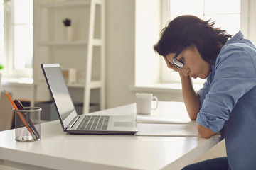 Exhausted young woman working on difficult task in front of laptop at home office. Freelancer feeling tired at workplace