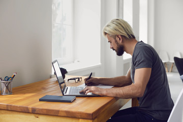 Young guy writing down main points from online business conference or educational webinar at desk indoors