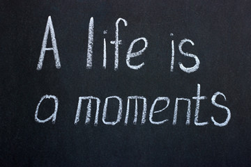 
The inscription "life is a moment". Chalk lettering on a dark board
