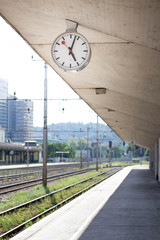 Train station clockon the platform with railroad tracks in the background, isolated.