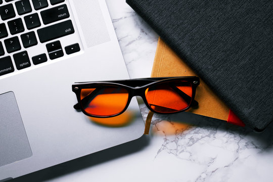 Desk With Laptop, Notebook, Tablet, And Blue Light Blocking Glasses. 