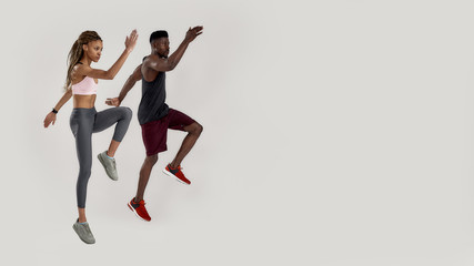 Fototapeta na wymiar Full length shot of young muscular african american man and sportive mixed race woman looking focused while jumping, exercising isolated over grey background. Sports and workout concept