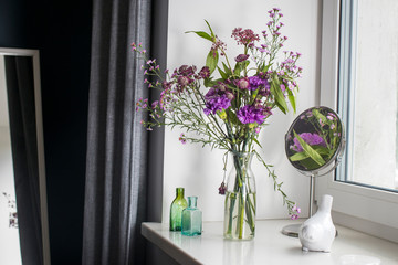 Autumn bouquet of astrantia, purple carnations and aster in a vase-bottle on the windowsill as interior decoration
