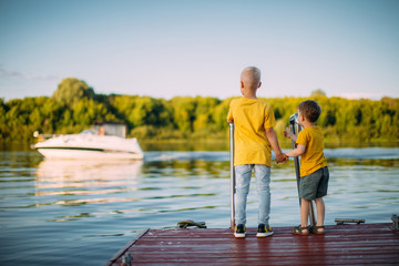 Cool kids brothers holding hands and staying on dock look at the boat on the river. Back view