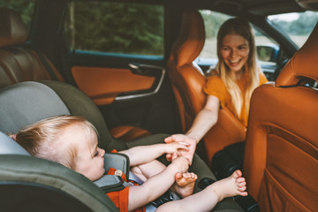 Family child in car holding mother hand baby sitting in safety seat mom driver on road trip...