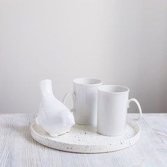 White porcelain cups and figurine of a bullfinch bird on a tray on wooden gray table.