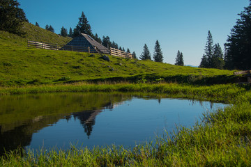 Panorama of typical wooden houses or cottages on the Velika planina or Mala Planina plateau in Slovenia on a hot sunny summer day with clear blue skies and lush green grass.