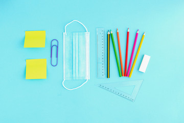 Medical face shield and colored pencils, paper clips and stickers on a light blue background. Back to school after the pandemic, office work during the quarantine period.
