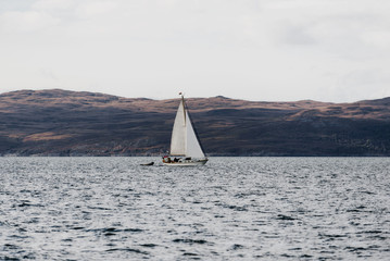 White yacht sailing near the rocky shores (cliffs) of the west coast of Jura island, a view from...