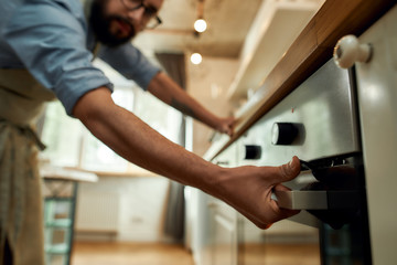 Cropped shot of man, professional cook opening electric oven, while preparing dinner at home. Hobby, lifestyle