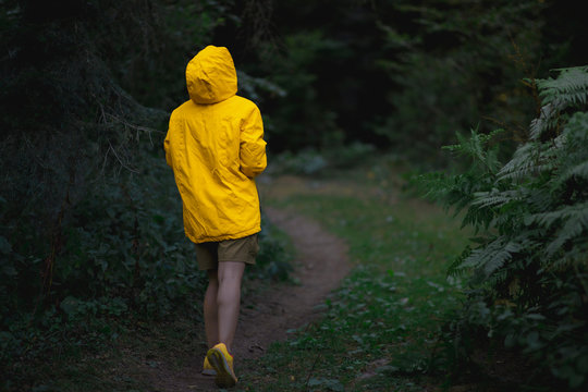 A backshot of jogger woman in a forest with yellow jacket in moody folk green tones.