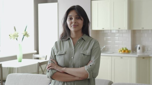 Smiling confident young pretty indian ethnic woman looking at camera standing alone at home in apartment kitchen arms crossed. Happy beautiful single millennial lady in India indoor, headshot portrait