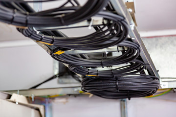 Cable management. Working wires, black cables wound into a coil, a circle. Rings of coiled wires, wire roll on cable ladder on the ceiling. Horizontal orientation.