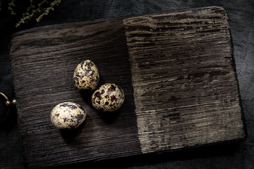 Three quail eggs on a dark wooden chopping board. Copy space