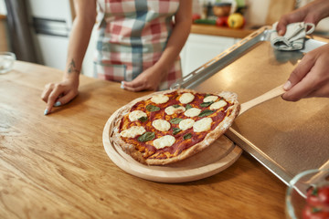 The pizza is arriving. Man, cook taking hot freshly baked pizza out of tray. Couple making pizza together. Hobby, lifestyle