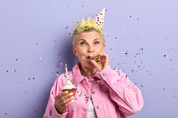 senior woman creating festive atmosphere, holiday mood, isolated blue background, studio shot.