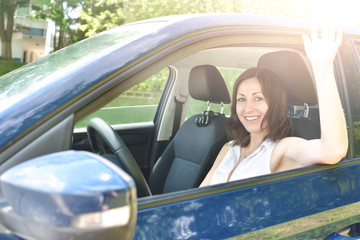 Fototapeta na wymiar Pretty girl is waving hand, giving smile to someone. say hello, Beautiful happy adult woman sits in the car and waving his hand in greeting