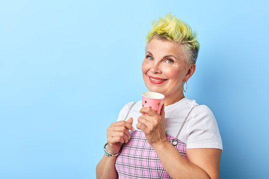 Happy Glamour Senior Woman With Yellow Dyed Hair Drinking Coffee Isolated On Blue Background.copy Space. Lifestyle, Interest Free Time , Spare Time