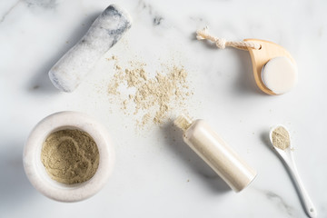 Homemade ubtan face mask preparation. Bowl with ubtan powder,, bottle, spoon with ingredients, cleansing brush on marble background. Natural organic spa beauty product.