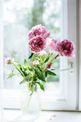 A beautiful pink bouquet of Peonies in a vase in a windowsill.