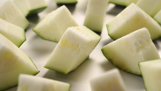 Pieces of fresh zucchini on a white surface close-up. Rotation. Vegetable Ingredients for Paleo and Keto Diets