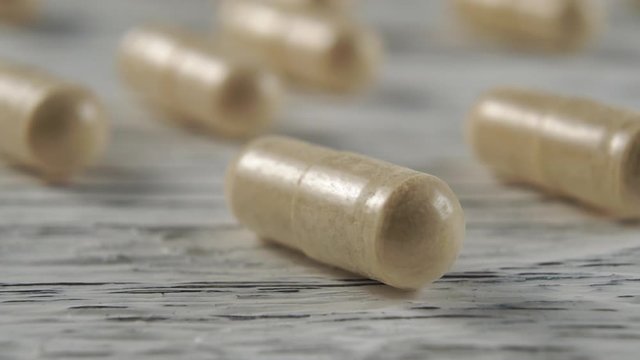 Beige herbal medical capsules on a wooden light background. Macro dolly shot