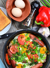 Scrambled eggs with fried sausages, onions, sweet red peppers, all in a frying pan.