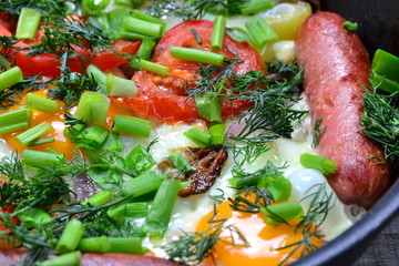 Scrambled eggs with fried sausages, onions, sweet red peppers, all in a frying pan.