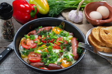 Scrambled eggs with fried sausages, onions, sweet red peppers, all in a frying pan.
