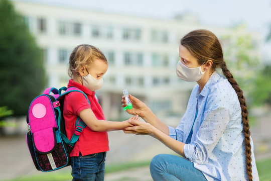 A parent treats her child's hands with antiseptic after school both wear a mask