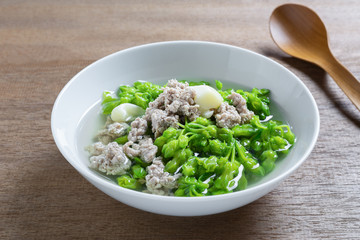 close up of cowslip creeper clear soup with pork minced in a ceramic bowl on wooden table. homemade style healthy food concept.