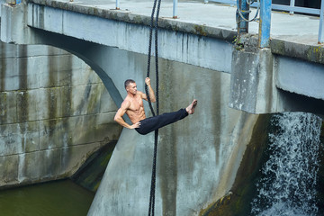 an athletic person performs dangerous exercises on a gymnastic rope. in the background is a dam...