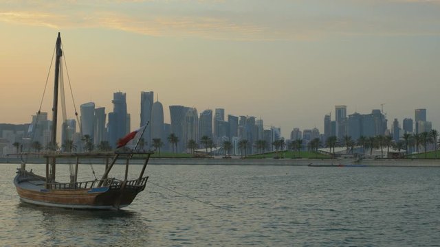 Doha skyline from Museum of Islamic Art Park sunset shot showing dhow with Qatar flag in the Arabic gulf  in foreground and clouds in the sky in background