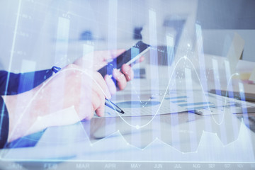 Double exposure of man's hands holding and using a phone and financial graph drawing. Analysis concept.