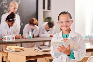 Happy cute pupil of secondary school in whitecoat and eyeglasses looking at you