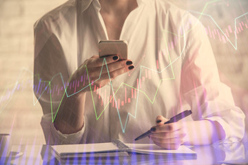 Double exposure of financial graph sketch hologram and woman holding and using a mobile device. Stock exchange concept.