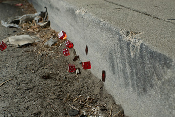 Red dice bouncing over a dirty street gutter and off the concrete curb.