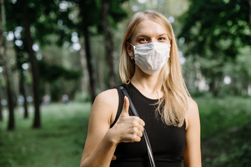 COVID-19 Optimistic young woman wearing protective mask avoiding Coronavirus disease 2019 showing thumbs up in city street